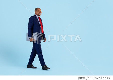 Mature african american businessman in suit walking confidently while holding laptop folder Mature african american businessman in suit walking confidently while holding laptop folder 137513645