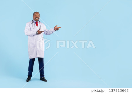 Black doctor in white coat with stethoscope pointing aside on blue background Black doctor in white coat with stethoscope pointing aside on blue background 137513665