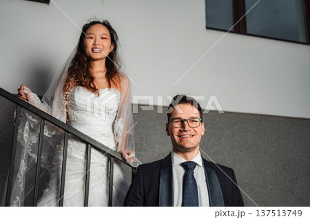 Interracial wedding couple smiling on stairs indoors Interracial wedding couple smiling on stairs indoors 137513749