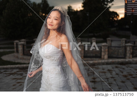 Asian bride smiling wearing wedding dress and veil in sunset lig Asian bride smiling wearing wedding dress and veil in sunset lig 137513750