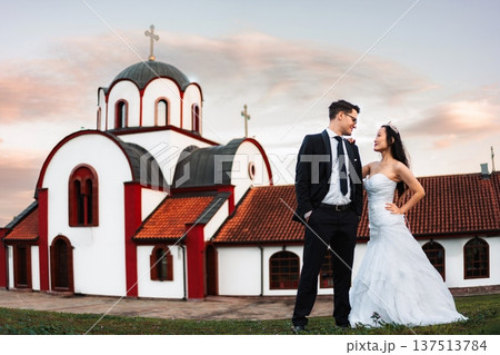 Interracial wedding couple standing outside Orthodox church at s Interracial wedding couple standing outside Orthodox church at s 137513784