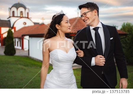 Interracial couple celebrating wedding day with church in backgr Interracial couple celebrating wedding day with church in backgr 137513785