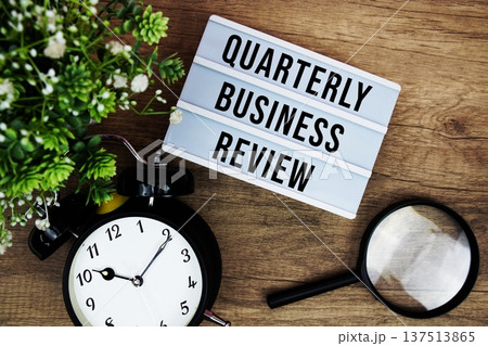 QBR Quarterly Business Review text in lightbox with magnifying glass and alarm clock flat lay on wooden background 137513865