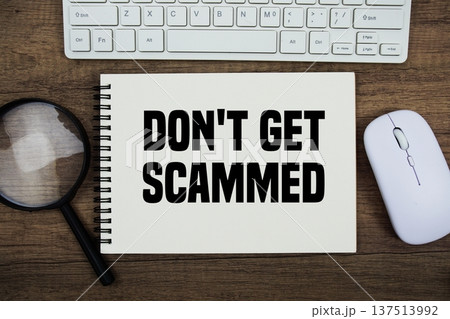 Don't Get Scammed text written on notepad with keyboard, optical mouse and magnifying glass on wooden background; Don't Get Scammed text written on notepad with keyboard, optical mouse and magnifying glass on wooden background; 137513992