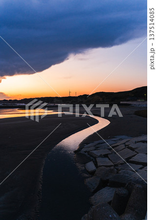 夕暮れの砂浜を流れて海へ向かう川 137514085