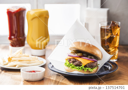 包装紙に包まれたチーズバーガーとポテトとドリンクのランチ 137514701