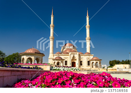 Architectural view of the Said Bin Taimur Mosque in Muscat, Oman, featuring twin minarets, domes, and colorful flower beds in the foreground under a clear blue sky. Architectural view of the Said Bin Taimur Mosque in Muscat, Oman, featuring twin minarets, domes, and colorful flower beds in the foreground under a clear blue sky. 137516938