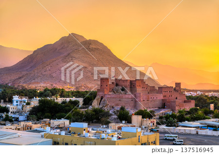 The majestic Nakhal Fort perched on a rocky outcrop against the backdrop of Hajar Mountains and a warm sunset sky in Oman. 137516945