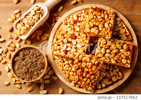 Brazilian peanut brittle prepared with roasted peanuts and caramelized brown sugar, served on a wooden plate on a rustic table and accompanied by peanut kernels. 137517662