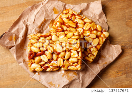 Two pieces of Brazilian peanut brittle made with roasted peanuts and golden caramel, on kraft paper on a rustic wooden table 137517671