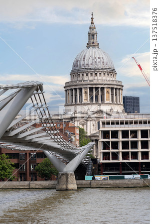 Historic architecture of St Paul Cathedral in London rises behind Millennium Bridge with pedestrians in the foreground beneath dramatic clouds in the sky. Historic architecture of St Paul Cathedral in London rises behind Millennium Bridge with pedestrians in the foreground beneath dramatic clouds in the sky. 137518376