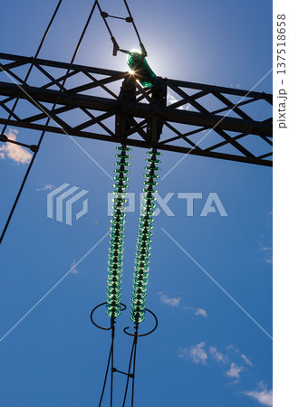Vertical view of suspended glass insulators on high-voltage lines at a transformer substation, without people, at daytime, on background of blue sky Vertical view of suspended glass insulators on high-voltage lines at a transformer substation, without people, at daytime, on background of blue sky 137518658