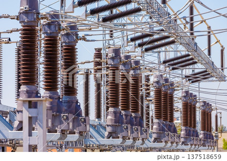 Close up view of various elements and high-voltage insulators of a transformer substation, without people, at daytime on background of blue sky Close up view of various elements and high-voltage insulators of a transformer substation, without people, at daytime on background of blue sky 137518659