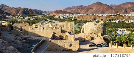 View of the ancient clay ruins and fortification walls of Fanja Fort overlooking the lush palm oasis and residential town in the Ad Dakhiliyah region, Oman 137518794