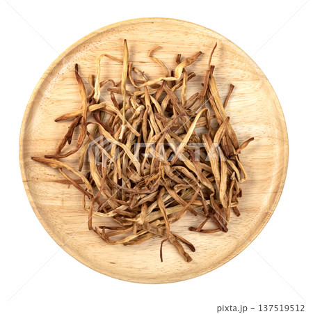 Top view of dried lily buds on a round wooden plate isolated. Traditional Chinese golden needle lily flowers used as a healthy culinary ingredient or herbal medicine. 137519512