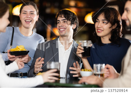 Group of positive young friends talking cheerfully and drinking beer at table in bar 137520914