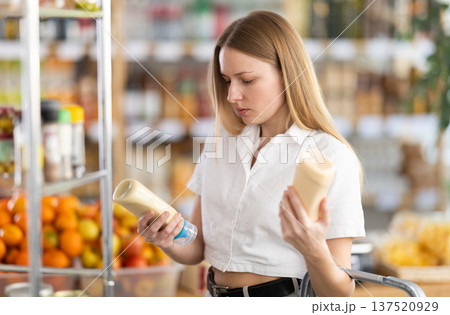 Choose food in supermarket - woman chooses mayonnaise to buy in the grocery department section of store Choose food in supermarket - woman chooses mayonnaise to buy in the grocery department section of store 137520929