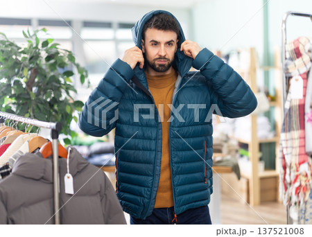 Young man trying on down jacket in store 137521008