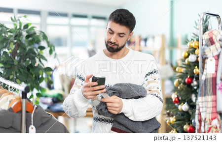 man holds a mobile phone and uses a barcode to pay for a sweater 137521143