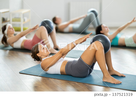 Young woman with athletes group hold fitball in lap knee , raise and lower torso Young woman with athletes group hold fitball in lap knee , raise and lower torso 137521319