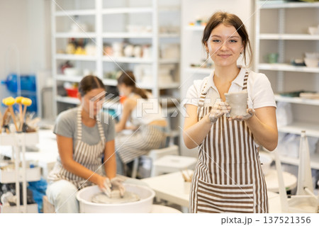 Girl takes break, stands and rests, waves hello with her hands stained with clay during pottery class 137521356
