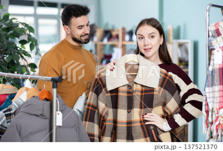 Woman choose plaid coat, man help, mutual family shopping Woman choose plaid coat, man help, mutual family shopping 137521370