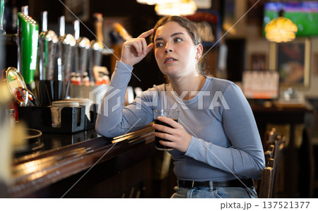 Young woman sitting in bar and drinking beer 137521377