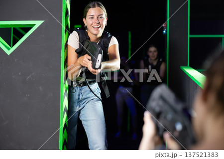 Team of young girlfriends play laser tag in labyrinth. Girls spend time actively Team of young girlfriends play laser tag in labyrinth. Girls spend time actively 137521383