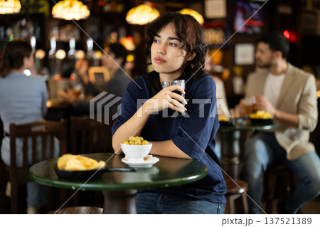 Young woman sitting in bar and drinking beer Young woman sitting in bar and drinking beer 137521389