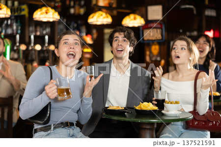 Group of emotional football fans watching match of favorite team at table in sports bar, and screaming chants together Group of emotional football fans watching match of favorite team at table in sports bar, and screaming chants together 137521591
