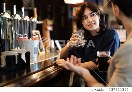 Young woman drinks beer and talks to man at bar Young woman drinks beer and talks to man at bar 137521595