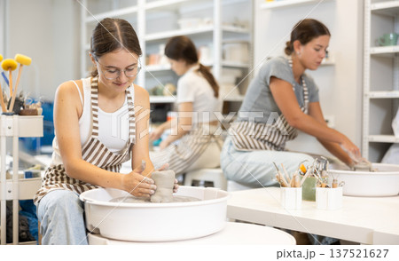Three young women sits near potter wheel and makes clay crafts 137521627