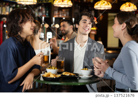 Two women actively chatting with a guy in a bar with a glass of beer 137521676