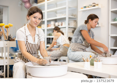 Three young women sits near potter wheel and makes clay crafts 137521679