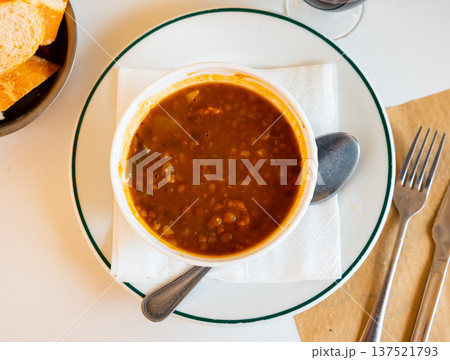 Spicy stewed lentils with suasage and vegetables with thick tomato sauce served in white plate. Spanish cuisine 137521793