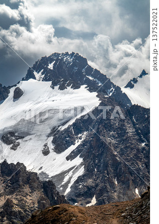 Majestic view of Ordzhonikidze Peak in Trans-Ili Alatau near Almaty. High mountain rocks covered with snow and glaciers under a dramatic cloudy sky. Popular destination for student hiking trips. 137522021