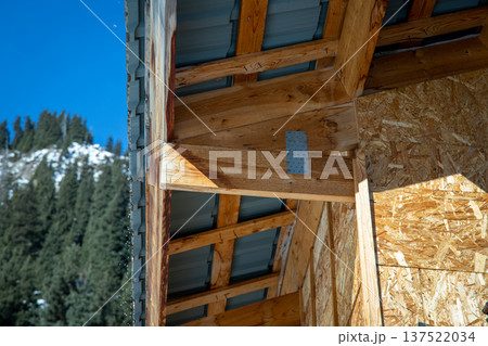Close-up of a roof overhang construction showing wooden rafters, OSB sheathing, and metal roofing sheets under a clear blue sky. 137522034