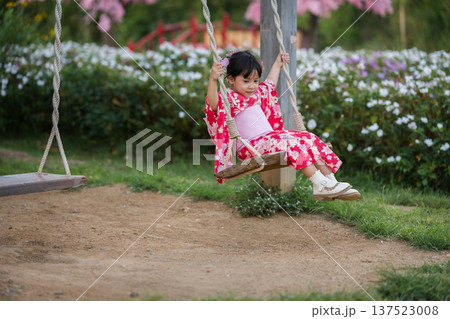 preschool child girl in yukata (kimono dress) playing on wooden swing in flower garden preschool child girl in yukata (kimono dress) playing on wooden swing in flower garden 137523008
