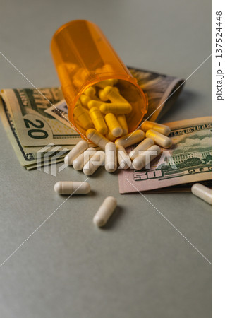 Pills spill from a bottle next to money on a plain surface Pills spill from a bottle next to money on a plain surface 137524448
