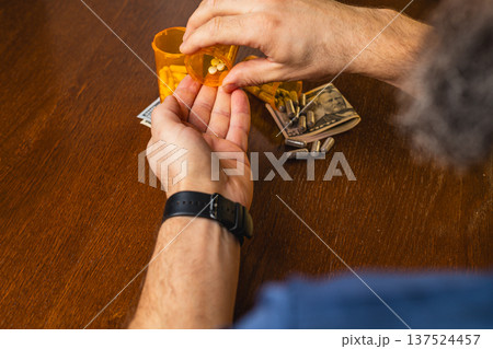 Man holds pills in hand with a prescription bottle and money on table Man holds pills in hand with a prescription bottle and money on table 137524457