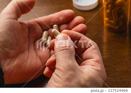 Person holds a supplement capsule above other capsules on a wooden table 137524469