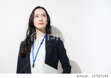白背景でパソコンを持つ名札をするビジネススーツを着たカッコイイ女性　未来や目標を見上げるイメージ 137525194
