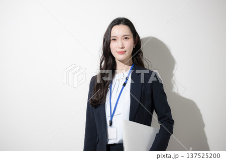 白背景でパソコンを持つ名札をするビジネススーツを着たカッコイイ女性　未来や目標を見上げるイメージ 137525200