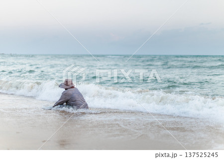 Local resident collecting shells in shallow sea waves on tropical beach 137525245