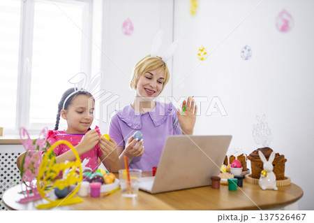 A mother and daughter enjoy decorating Easter eggs together while participating in an online class, fostering family bonding and festive creativity 137526467