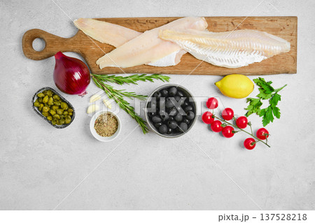 Fresh fish fillets and cooking ingredients on a wooden cutting board in a kitchen setting 137528218