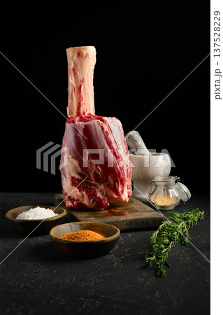 Preparing a large meat cut with spices, salt and herbs on a wooden board in dark setting 137528229