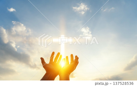Human hands reaching up to a glowing cross in the sky. Concept of faith, hope, christianity, spirituality, divine light, blessing, and religious belief. Human hands reaching up to a glowing cross in the sky. Concept of faith, hope, christianity, spirituality, divine light, blessing, and religious belief. 137528536