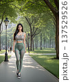 街中の緑地の遊歩道を歩くスポーツウエアを着た女性（左配置） 137529526
