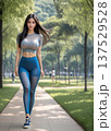 緑地公園の林中の遊歩道を歩くスポーツウエアを着た女性 137529528